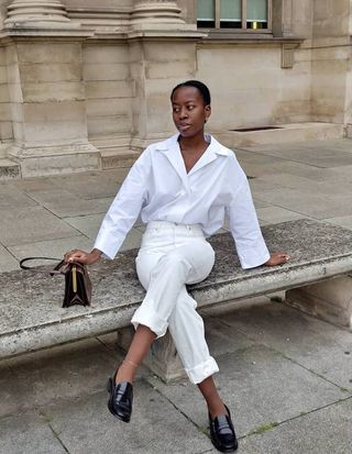 Sylvie Mus wearing white jeans, a white button-down top, black loafers, and a shoulder bag.