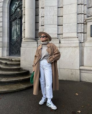 Olivia Faeh wearing white jeans, New Balance sneakers, a camel coat, a turtleneck sweater, and a hat.