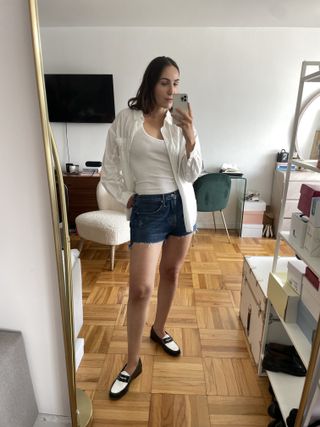 Anna LaPlaca wearing Good American Good '90s Shorts, penny loafers, a white button-down shirt, and a white tank top.