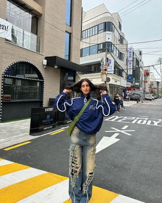 Ana wearing ribbed jeans, a blue track jacket, and a green crossbody bag.