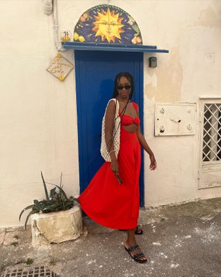 Chrissy Ford wearing a red dress, black sandals, a crochet bag, and black sunglasses.