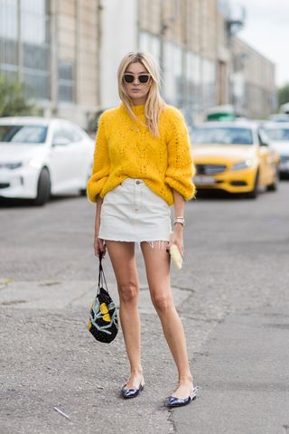 Woman wearing a yellow sweater with a white denim miniskirt and slingback flats.