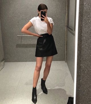 a woman wears a white crewneck T-shirt with a black miniskirt and black ankle boots