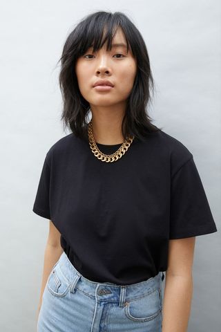 a model wears a black T-shirt with a gold chain necklace