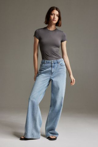 a model wears a gray T-shirt with baggy blue jeans