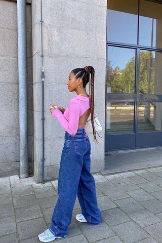 a photo showing how to wear wide jeans with a woman wearing wide leg jeans with chunky white sneakers and an open back top