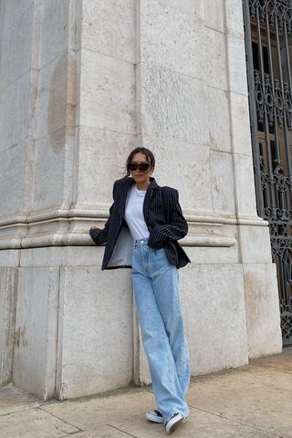 Debora wears a black blazer, white t-shirt, wide-leg jeans, and black sneakers.