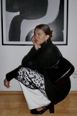 a photo showing how to wear dresses in the winter with a woman wearing a black turtleneck over a sheer sequin dress that's layered over white trousers with black mary jane pumps