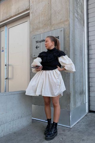 a photo showing how to wear dresses in the winter with a woman wearing a white puff sleeve dress under a black sweater dress styled with black combat boots