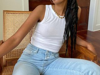 Fashion influencer Claire Most sits in a modern chair wearing a white tank top, chain necklace, and high-waisted jeans