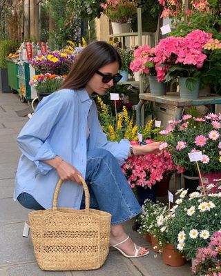 Woman wearing a blue button-down and jeans kneeling in front of bouquets of flowers.