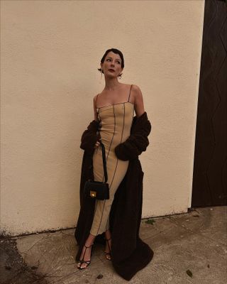 a photo showing black tie attire for women with a woman wearing nude gown with a long black coat and black strappy sandals