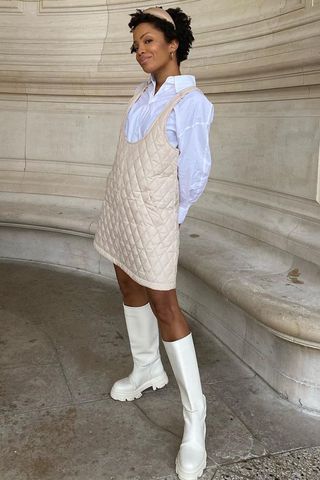 a photo of a woman's outfit with flat knee-high boots and a tan leather mini dress styled over a white button-down