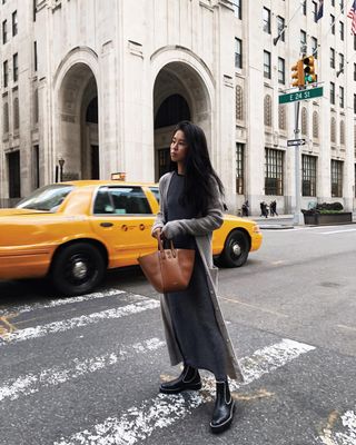 Kristen wearing a grey maxi skirt, black lug-sole boots, a long cardigan, and a brown leather tote bag.