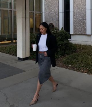 Dawn wears a black blazer, white shirt, brown belt, gray denim skirt, and gucci slingback heels.