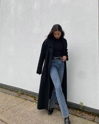 woman's outfit with bootcut denim, black ankle boots, black sweater, and black coat