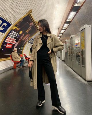 woman's outfit with black bootcut jeans, black shirt, black sneakers, and trench coat