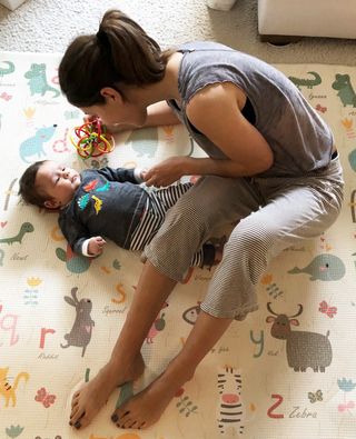 best postpartum clothes shown on a woman sitting on the floor with her baby wearing a gray t-shirt and lightweight pajama bottoms