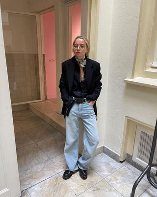 a woman's outfit with baggy jeans styled with black loafers, a black blazer, tank, belt, and printed black and white scarf