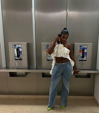 a woman's outfit with baggy jeans styled with a white ruffle halter crop top, green heels, and silver hoop earrings