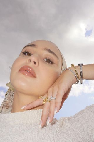 Maria Alia wearing a white top, silver and gold bracelets, and multiple rings.