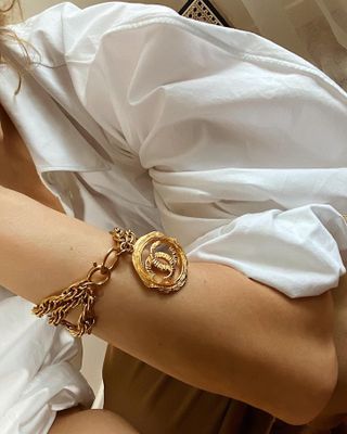 A woman wearing a white top and a gold Chanel bracelet.