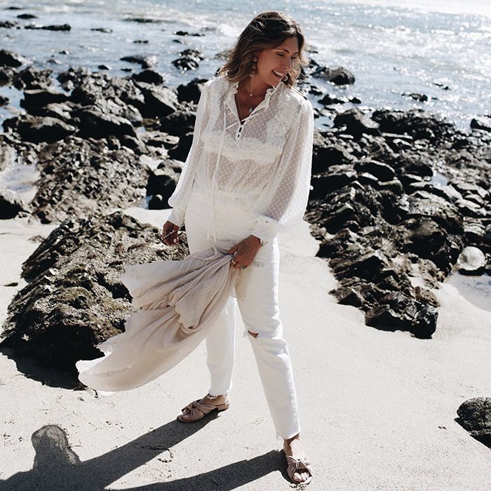 Melissa Meyers wearing a white blouse and white pants with flat sandals at the beach.