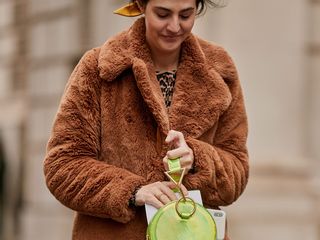 Woman wearing a brown furry coat and carrying a neon green designer bag.