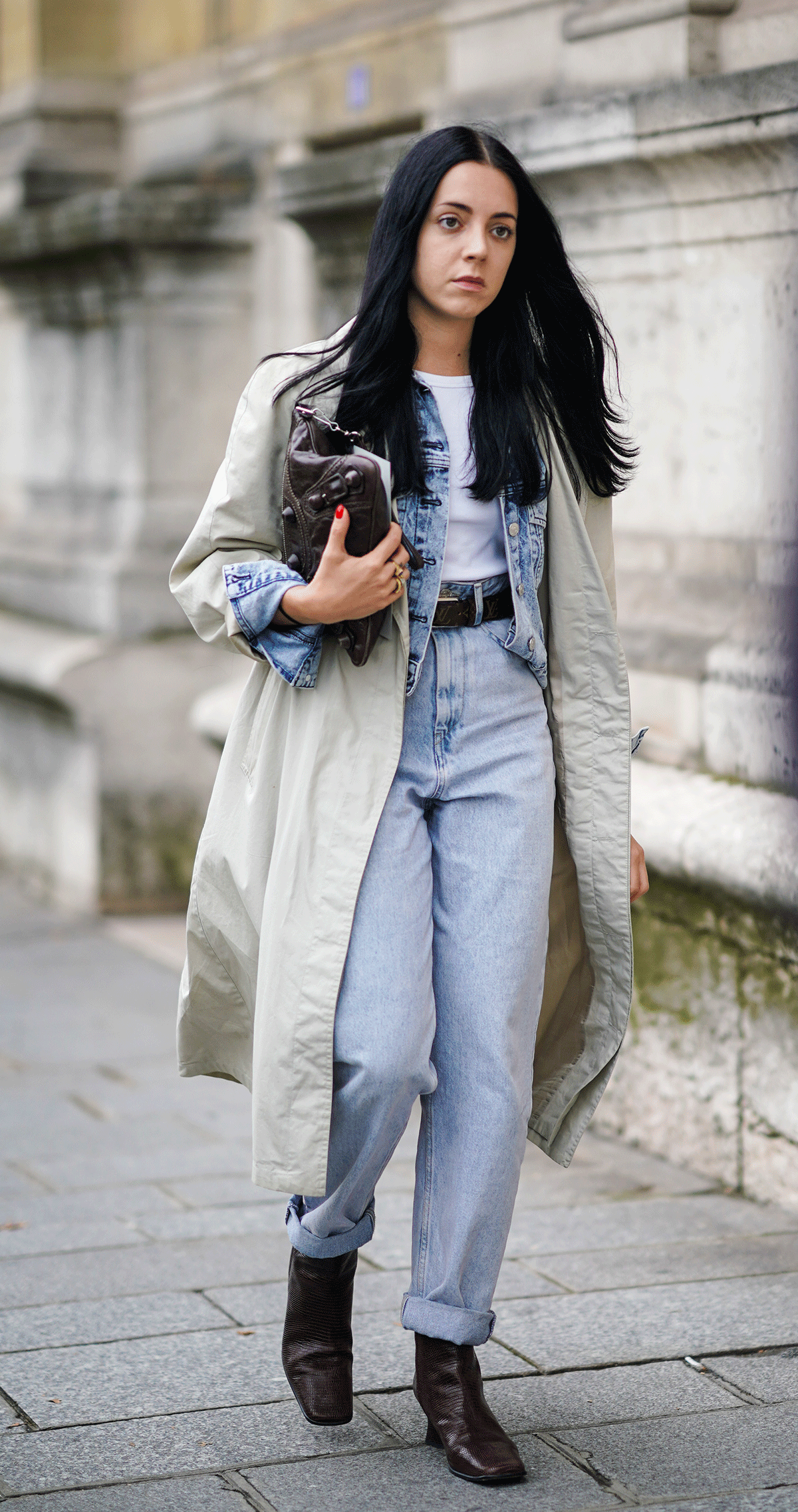 a photo showing how to style straight-leg jeans with a woman wearing a trench coat over a denim jacket and white t-shirt with jeans and ankle boots