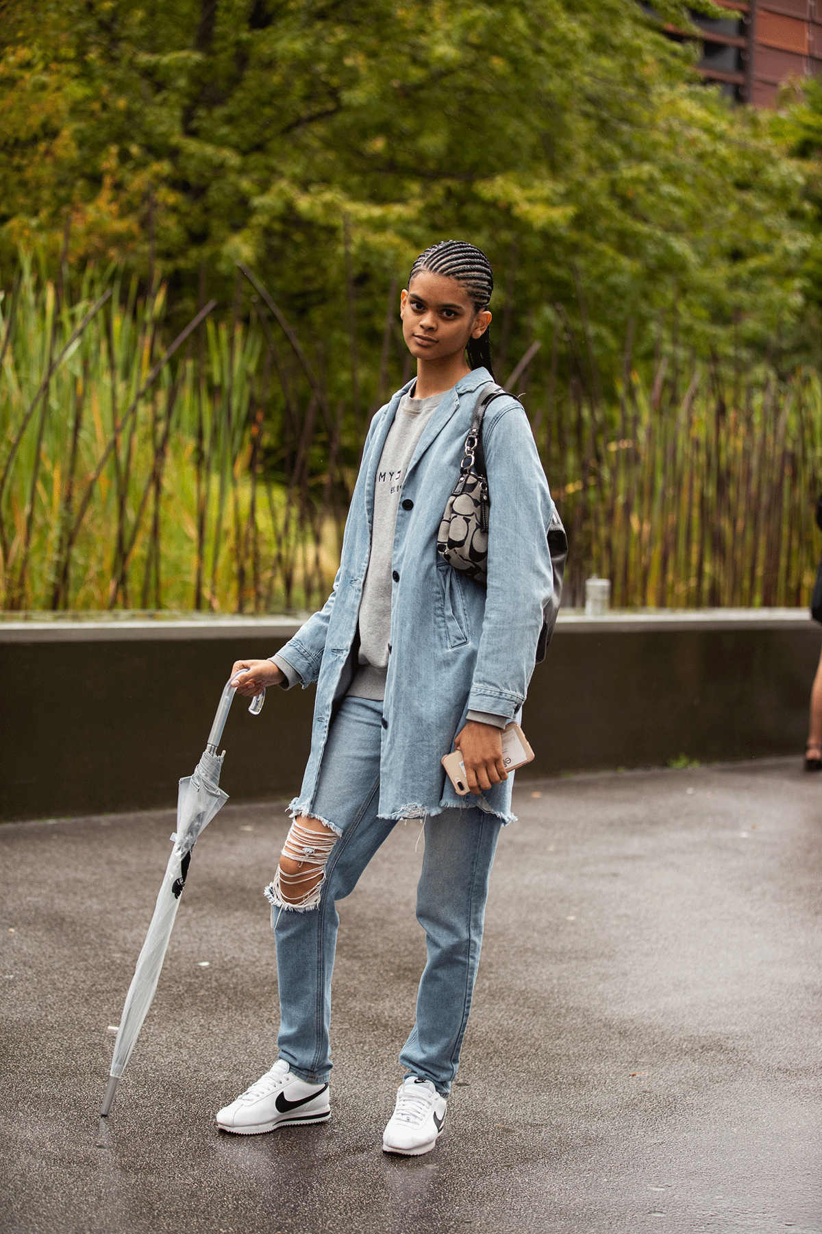 a photo showing how to style straight-leg jeans with a woman wearing a denim shirt over a gray sweatshirt with jeans and sneakers