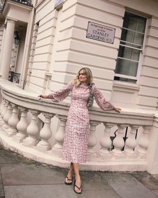 Anne wears a pink printed maxi dress, printed handbag, and black sandals.