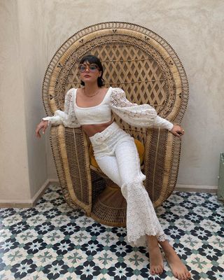 Maria wears a lace cropped top, lace pants, and circular red sunglasses.