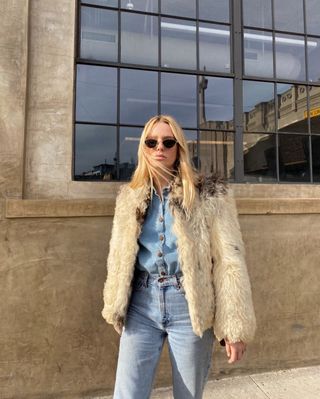 Megan wears a fur coat, denim top, denim pants, and sunglasses.