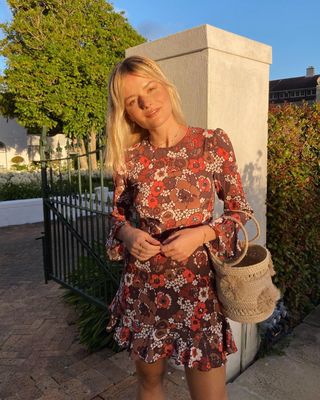 Sabina wears a floral mini dress and a straw bucket bag.