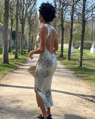 Woman wearing white backless maxi dress with black floral outline while walking in park.