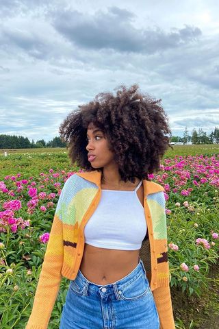 Claire wears a colorful cropped cardigan, white cropped tank top, and high-waisted jeans.