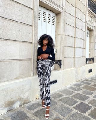 Andi wearing printed pants, a long-sleeve crop top, and white heels.