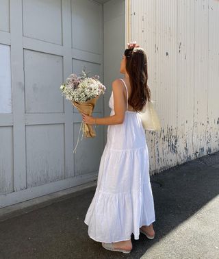 Emma Leger mengenakan gaun panjang putih berkibar dengan sandal datar.