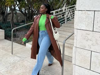A woman wearing cheap high waisted jeans with a green top and tan leather trench.