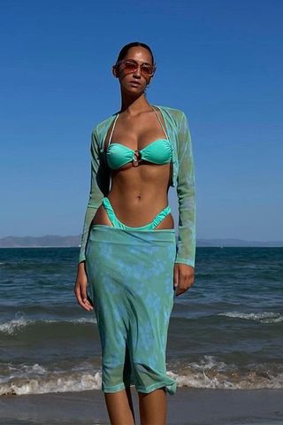 a photo of a woman's beach outfit with a mesh cardigan and bikini and mesh skirt and sunglasses