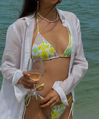 a photo of a woman's beach outfit with white button-down shirt over floral print bikini with pearl necklace