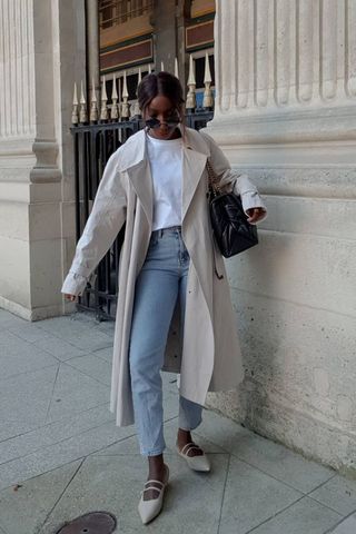 a photo of a woman's outfit with mary jane flats, jeans, a white t-shirt and a trench coat