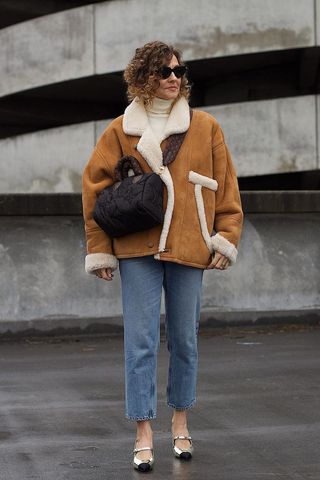 a photo of a woman's outfit with mary jane heels and jeans and a shearling jacket