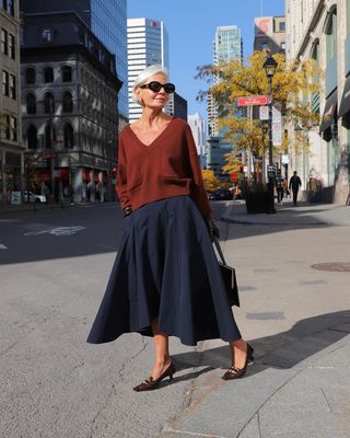 Grece wearing a midi skirt, red sweater, and black heels.