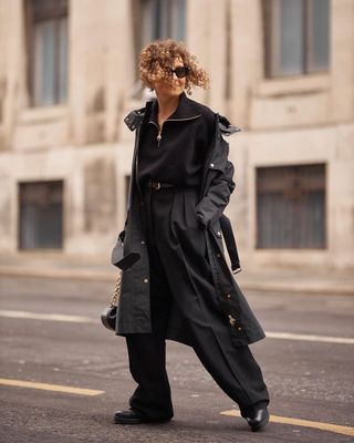 A woman wearing a black coat, black sweater, black pants, and black boots.