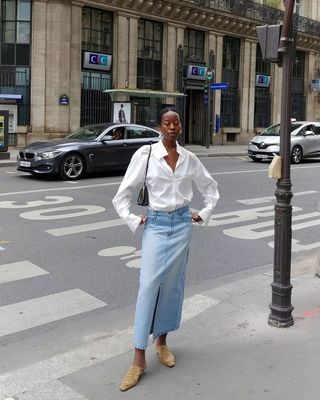 a photo of a woman's outfit with a long denim skirt and white button-down shirt and heeled mules