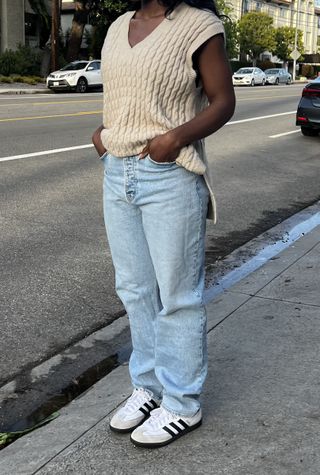 a photo of a woman wearing baggy denim jeans with white sneakers and a tan vest