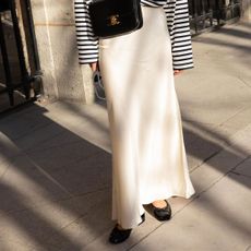 Woman wearing a silk maxi skirt with black ballet flats, a striped sweater, and a black Celine crossbody bag.