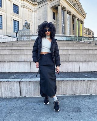 Ciara Cherise wearing a lightweight maxi skirt with sneakers, a crop top, and a puffer jacket.