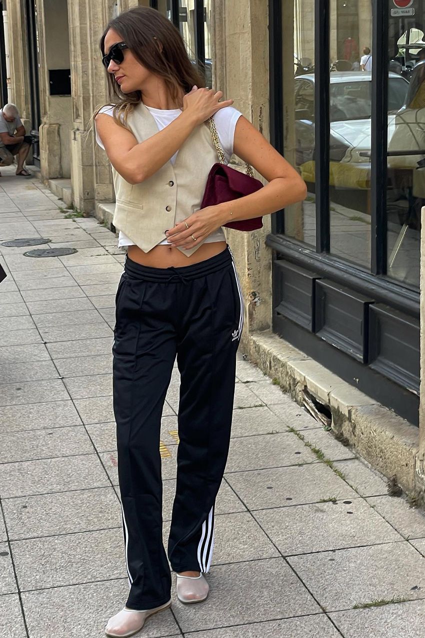 Anne-Laure Mais wears Dear Frances mesh ballet flats, adidas tracksuit trousers, a biege waistcoat and a white t-shirt.